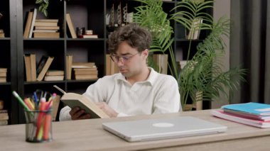 Young specialist reads a book in his free time from work using free time effectively for brain and new knowledge. Boy lectures a book at work in a modern office. Modern conditions for employees