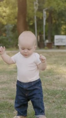 Bebek çimen ve yapraklarla meşgul, canlı bir açık havada dokuları ve renkleri keşfediyor, merakın ve duyusal keşfin özünü yakalıyor.
