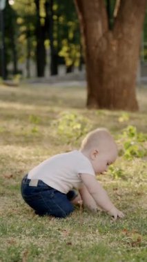 Bebek çimen ve yapraklarla meşgul, canlı bir açık havada dokuları ve renkleri keşfediyor, merakın ve duyusal keşfin özünü yakalıyor.
