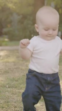 Bebek çimen ve yapraklarla meşgul, canlı bir açık havada dokuları ve renkleri keşfediyor, merakın ve duyusal keşfin özünü yakalıyor.
