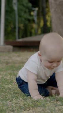 Bebek çimen ve yapraklarla meşgul, canlı bir açık havada dokuları ve renkleri keşfediyor, merakın ve duyusal keşfin özünü yakalıyor.