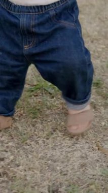 Bebek çimen ve yapraklarla meşgul, canlı bir açık havada dokuları ve renkleri keşfediyor, merakın ve duyusal keşfin özünü yakalıyor.