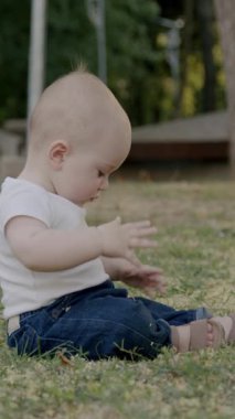 Bebek çimen ve yapraklarla meşgul, canlı bir açık havada dokuları ve renkleri keşfediyor, merakın ve duyusal keşfin özünü yakalıyor.