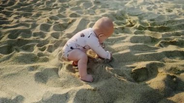 Infant is seated on sandy beach, engaged in playful activity with sand, enjoying warm sunlight and soft textures, creating delightful memories of childhood