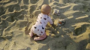 Infant is crawling on sandy surface, wearing cute animal-patterned outfit, exploring surroundings with curiosity, sunlight creating warm atmosphere and gentle shadows