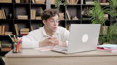 Student amazed and upset when he saw how much information and materials he has to study to prepare for exams. Young boy studying at an office table in front of a laptop