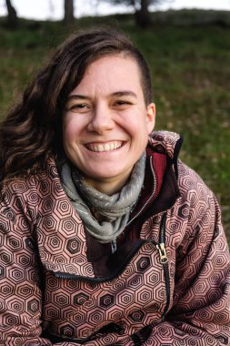 Genç bir kadın kameraya bakıp gülümsüyor.