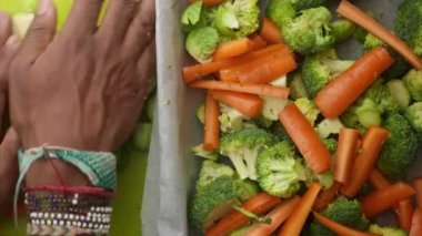 Fırın tepsisini doğranmış sebzelerle hazırlayan ellerin üst görüntüsü.