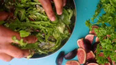 hands of male chef preparing healthy green salad with figs in kitchen, washing leafy greens