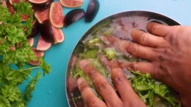 hands of male chef preparing healthy green salad with figs and walnuts in kitchen, washing leafy greens