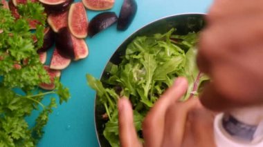 15 seconds video. Video shows a chef preparing a healthy green salad with salt, sliced figs in a kitchen.
