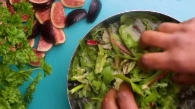 hands of male chef preparing healthy green salad with figs and walnuts in kitchen, washing leafy greens