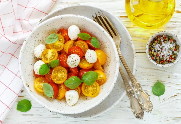 Delicious summer salad of yellow and red cherry tomatoes, mozzarella with Basil and spices. Caprese. Selective focus