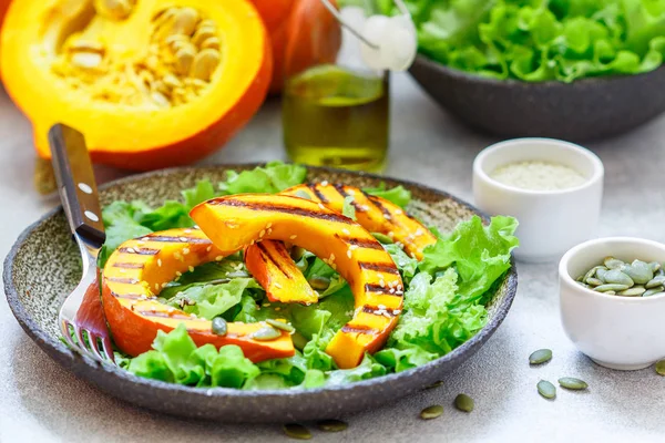 Delicious light salad of grilled pumpkin slices and lettuce with sesame seeds, lemon juice and olive oil. Healthy diet, vegetarian snack. Selective focus