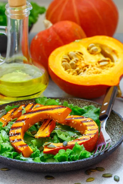 Delicious light salad of grilled pumpkin slices and lettuce with sesame seeds, lemon juice and olive oil. Healthy diet, vegetarian snack. Selective focus