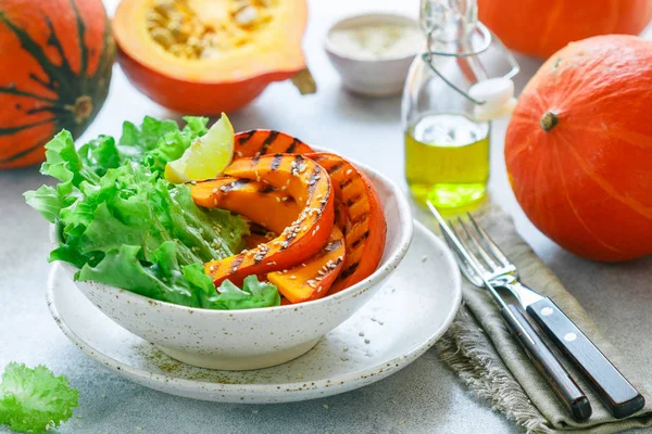 Delicious light salad of grilled pumpkin slices and lettuce with sesame seeds, lemon juice and olive oil. Healthy diet, vegetarian snack. Selective focus