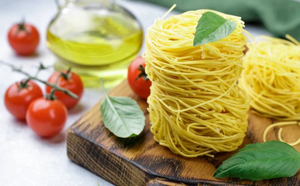 Raw Egg pasta nest - Homemade Capelli d\'angelo, Angel\'s hair. Italian Cuisine. Ingredients for a delicious dinner. Basil, vermicelli, tomatoes,  olive oil and spices on the table. Selective focus