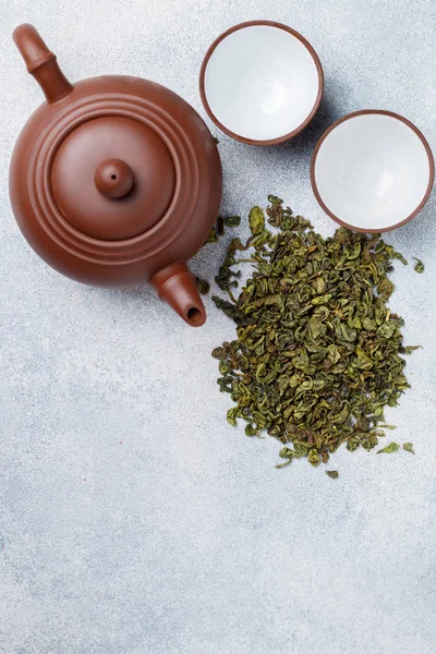 Dry green tea, kettle and two cups on grey concrete surface. Selective focus, top view and copy space