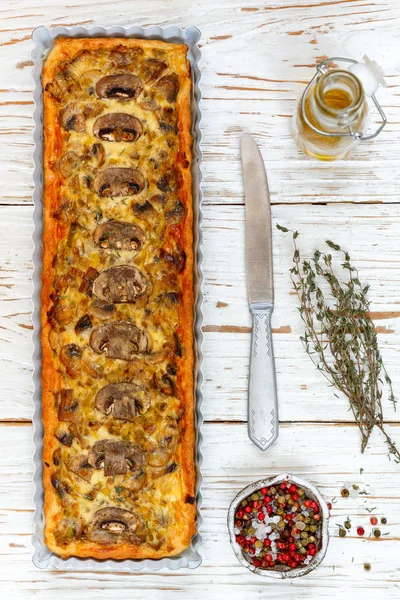 Homemade tart with mushrooms, leek, cheese and thyme on white rustic background. Traditional snack cake and a knife on the table. Selective focus