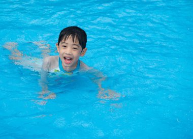 Mutlu Asyalı sevimli çocuk beş yaşında yüzüyor ve mavi berrak yüzme havuzunda oynuyor. Yaz tatilinde dinleniyor..