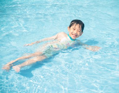 Mutlu Asyalı sevimli çocuk beş yaşında yüzüyor ve mavi berrak yüzme havuzunda oynuyor. Yaz tatilinde dinleniyor..