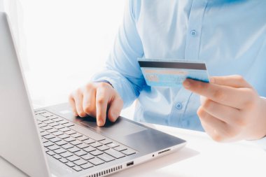 Mavi gömlekli bir adam elinde banka kartı olan bir dizüstü bilgisayarla çalışıyor. Uzaktan çalışma, uzaktan kumanda, online alışveriş, alışveriş