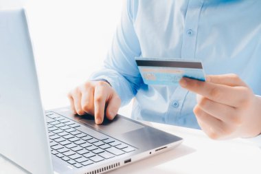 Mavi gömlekli bir adam elinde banka kartı olan bir dizüstü bilgisayarla çalışıyor. Uzaktan çalışma, uzaktan kumanda, online alışveriş, alışveriş