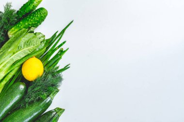 Yeşil sebzeler ve sarı limonlu açık arkaplan. Yukarıdan manzara. Sağlıklı beslenme. Metin için boş alan