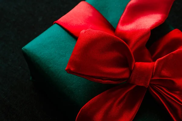 Close-up van de kerstgeschenkdoos bovenop. Groene geschenkdoos met een zijden rode strik op een donkere achtergrond — Stockfoto