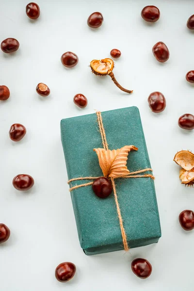 Gift box with a dry autumn leaf with many chestnut fruits on a light background