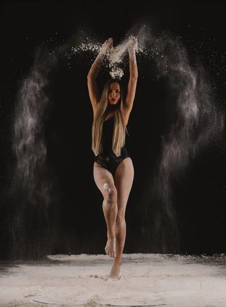 Bella sensuale ballerina slim fit nel corpo nero con lunghi capelli biondi gettando polvere, farina, polvere su sfondo nero. — Foto Stock