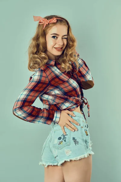 곱슬곱슬 한 금발 머리에 빨간 체크무늬 활과 청바지 바지를 입은 성냥팔이 소녀. — 스톡 사진