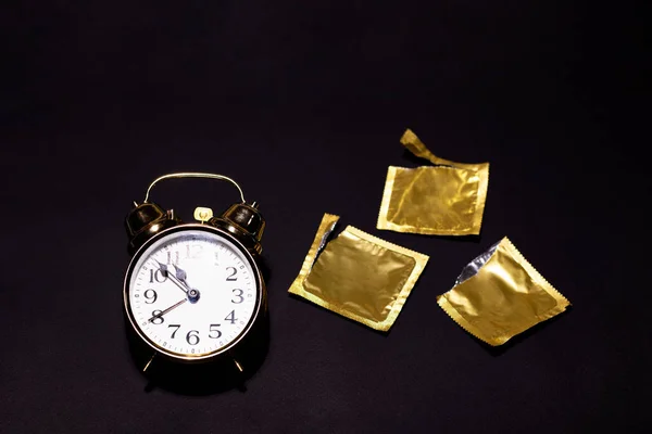 A gold watch next to opened condoms on a black background — Stock Photo, Image