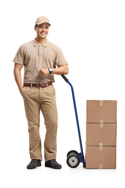 Full length portrait of a delivery man leaning on a hand truck loaded with boxes isolated on white background