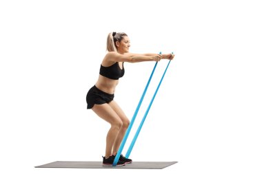 Tam uzunlukta profil atış bir hasır üzerinde duran ve beyaz arka plan üzerinde izole bir lastik bant ile egzersiz genç bir kadın