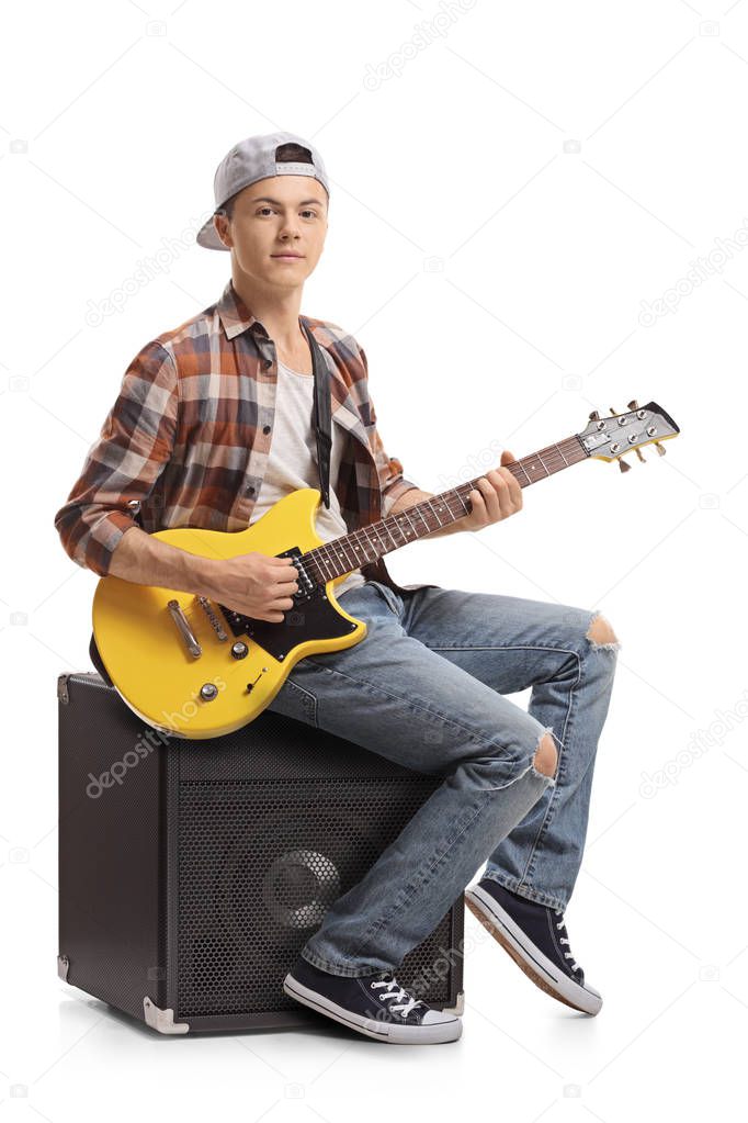 Teenage boy with an electric guitar sitting on an amplifier isolated on white background