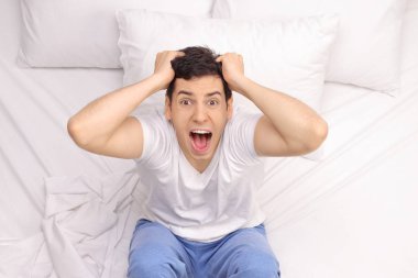 Young man suffering from insomnia sitting on a bed clipart