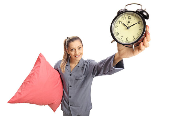 Young woman in pajamas holding a pillow and an alarm clock isolated on white background