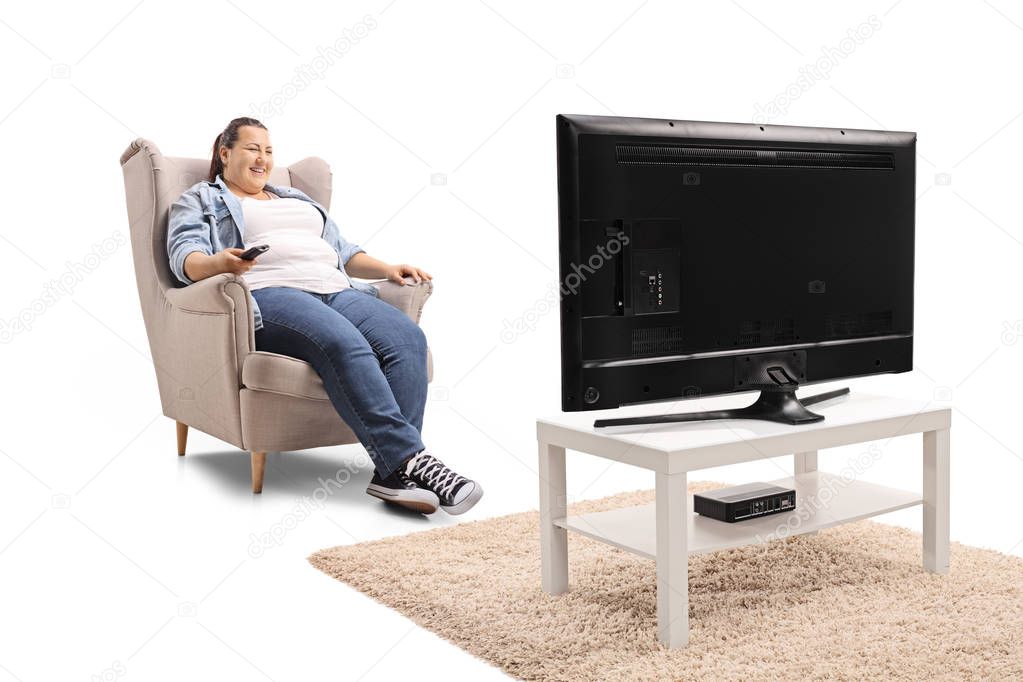 Young woman seated in an armchair watching television isolated on white background