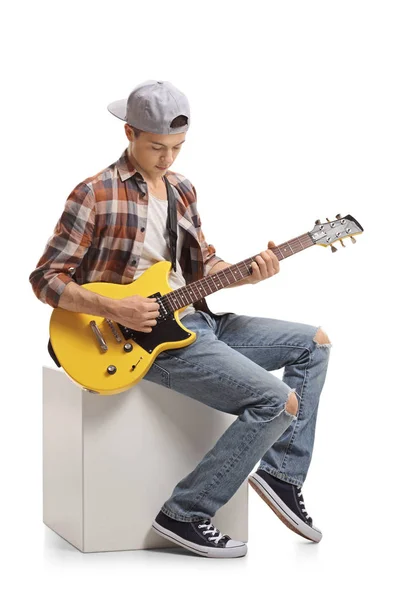 十几岁的男孩坐在立方体和演奏电吉他隔绝在白色背景上 — 图库照片