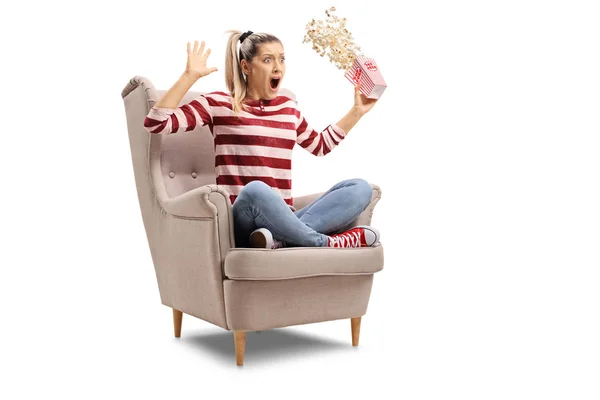 白い背景に分離された肘掛け椅子に座ってポップコーンの箱を持つ恐怖の若い女性 — ストック写真