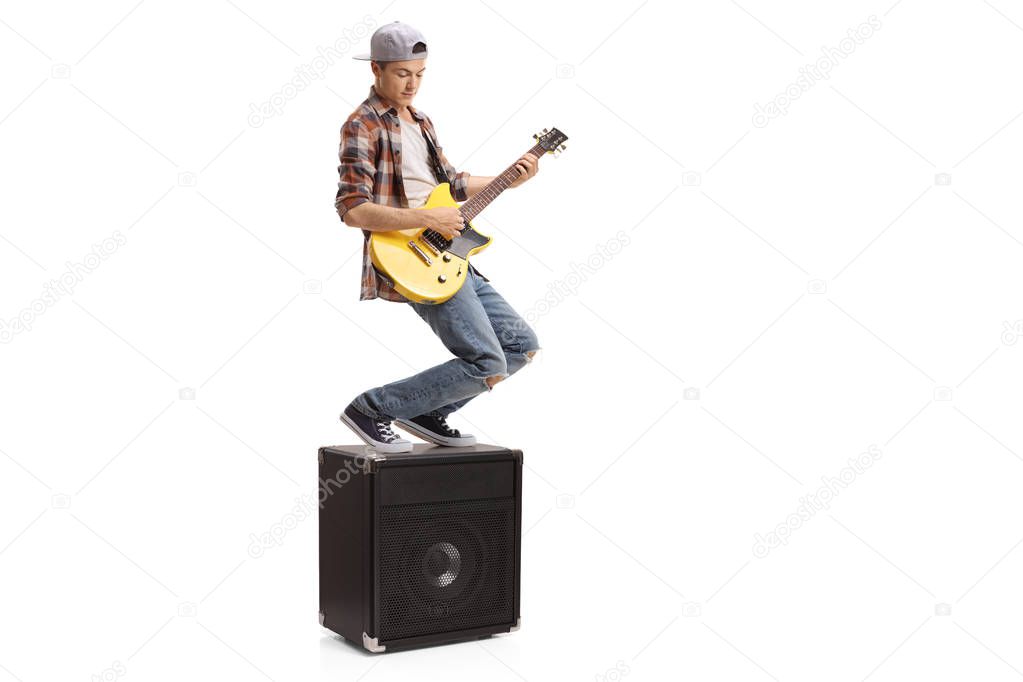 Teenage boy standing on an amplifier and playing an electric guitar isolated on white background