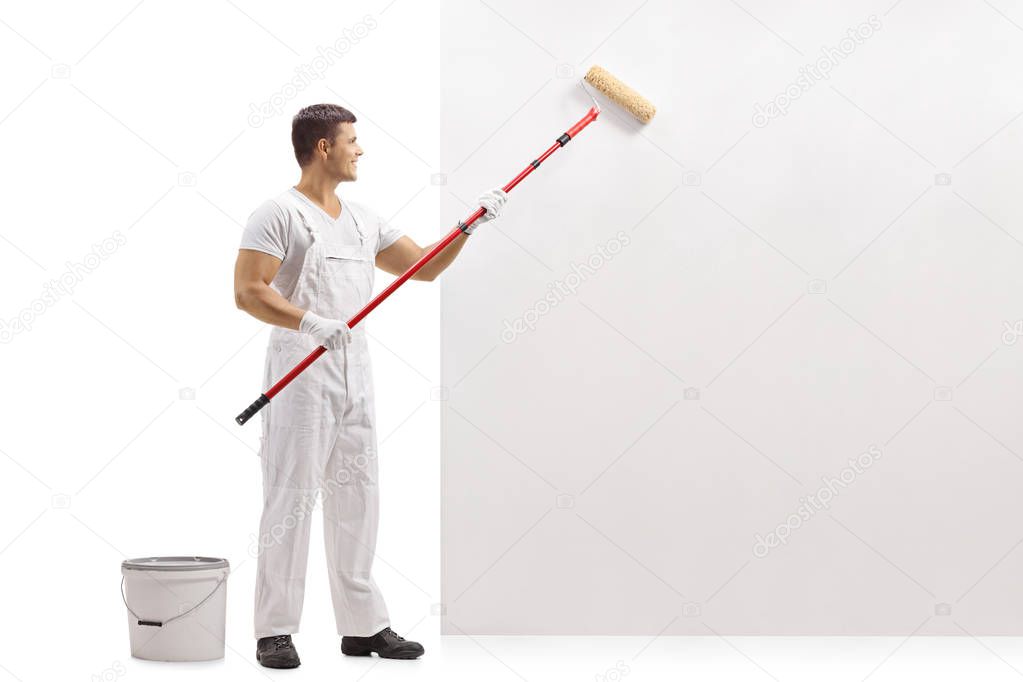 Full length profile shot of a painter painting a wall with a paint roller isolated on white background