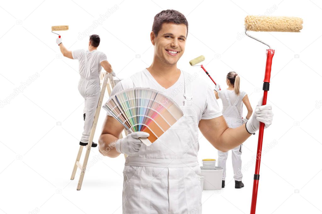 Painter holding a color swatch and a paint roller with two painters painting behind him isolated on white background