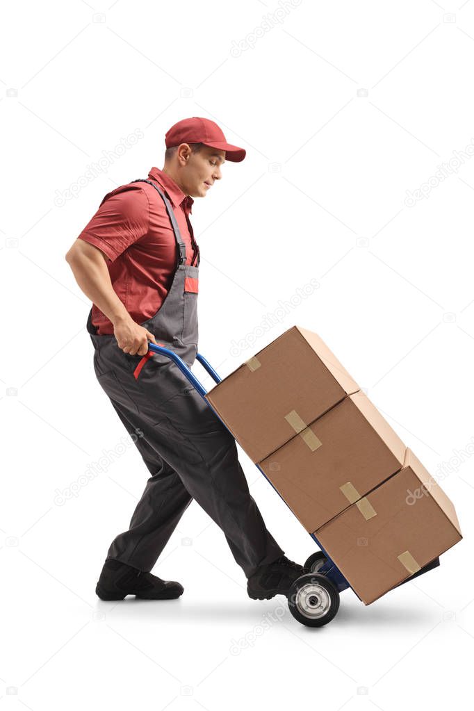 Full length profile shot of a mover with a hand truck loaded with cardboard boxes isolated on white background