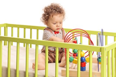 Beyaz arka plan üzerinde izole bir beşik oyuncaklarla oynayan erkek bebek