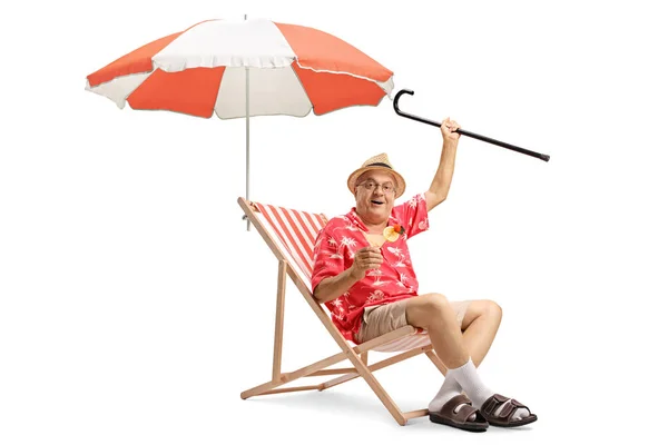 カクテルと白い背景に分離された傘を持ったデッキの椅子に座って杖うれしそうな高齢者の観光 — ストック写真
