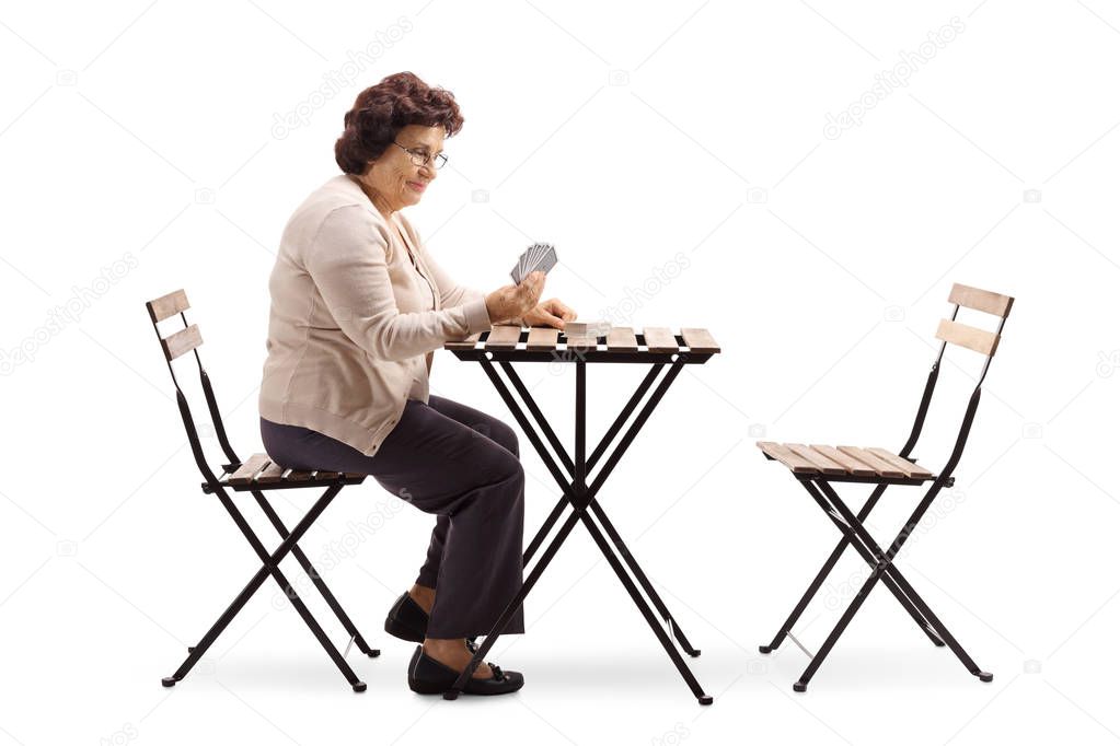 Senior lady sitting at a table and playing cards isolated on white background