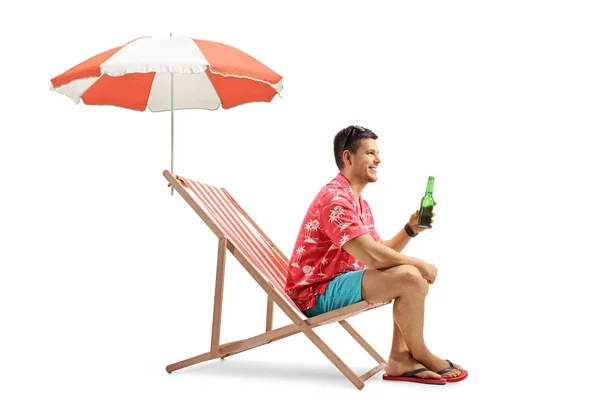 游客用一瓶啤酒坐在甲板椅上 用雨伞隔离在白色背景上 — 图库照片