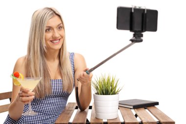 Bir masada bir kokteyl oturma ve beyaz arka plan üzerinde izole bir sopa ile bir selfie alarak genç kadınla